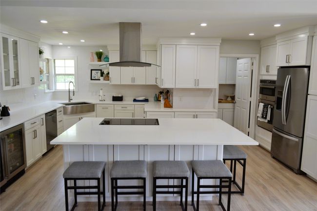 Kitchen featuring stainless steel appliances, wall chimney exhaust hood, open shelves, a kitchen breakfast bar, and beverage cooler | Image 8