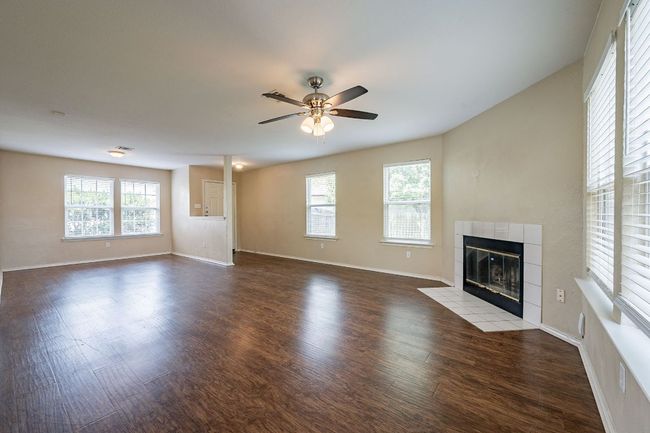 Unfurnished living room with a tiled fireplace, ceiling fan, wood finished floors, and baseboards | Image 5