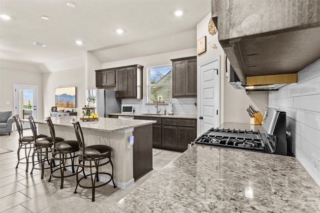 Kitchen with gas range, range hood, a center island, freestanding refrigerator, and a breakfast bar | Image 5