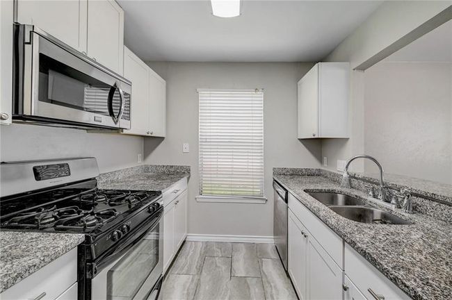 Kitchen featuring stainless steel appliances, a sink, baseboards, light stone counters, and white cabinets | Image 9