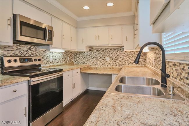 Kitchen with stainless steel appliances, a sink, light countertops, white cabinets, and crown molding | Image 23