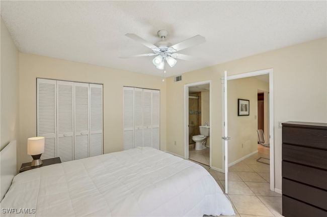 Bedroom featuring multiple closets, light tile patterned floors, ceiling fan, and ensuite bath | Image 17