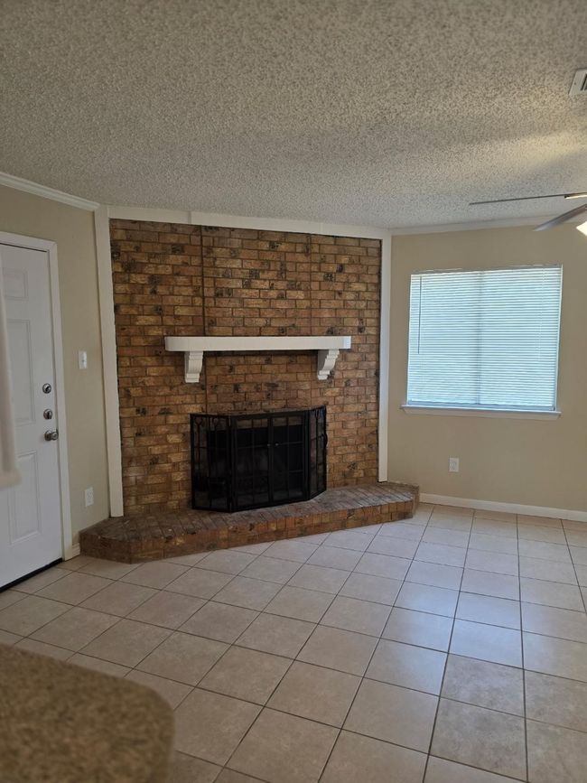 Unfurnished living room featuring a brick fireplace, tile patterned flooring, ornamental molding, a textured ceiling, and ceiling fan | Image 5