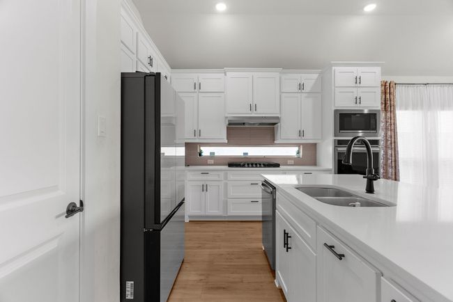 Kitchen with black appliances, a sink, white cabinetry, light countertops, and recessed lighting | Image 9