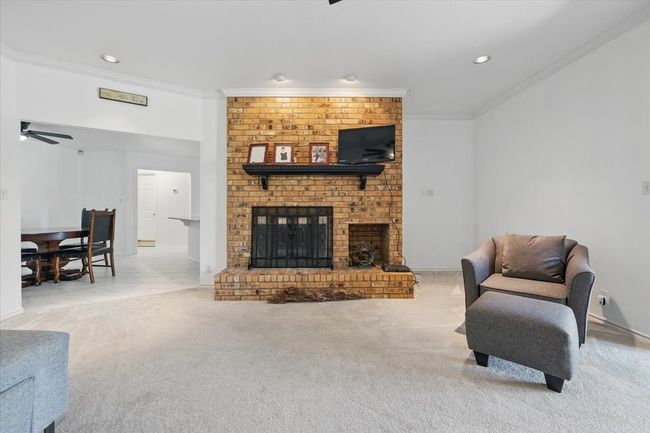 Carpeted living area with crown molding, a brick fireplace, recessed lighting, a ceiling fan, and baseboards | Image 9