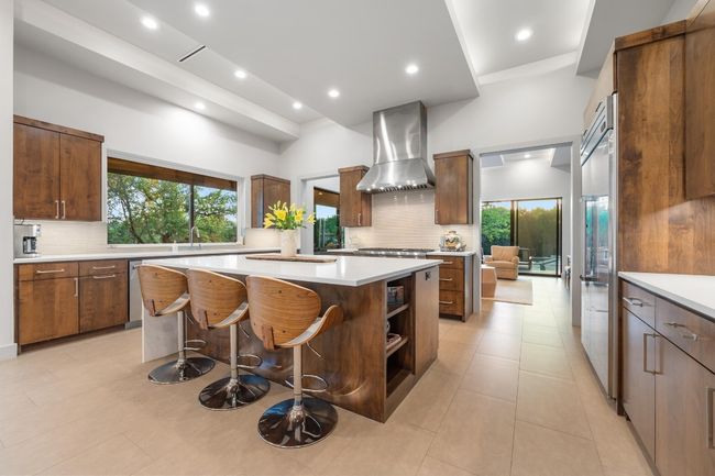 Kitchen with wall chimney exhaust hood, tasteful backsplash, a kitchen island, dishwasher, and light countertops | Image 11