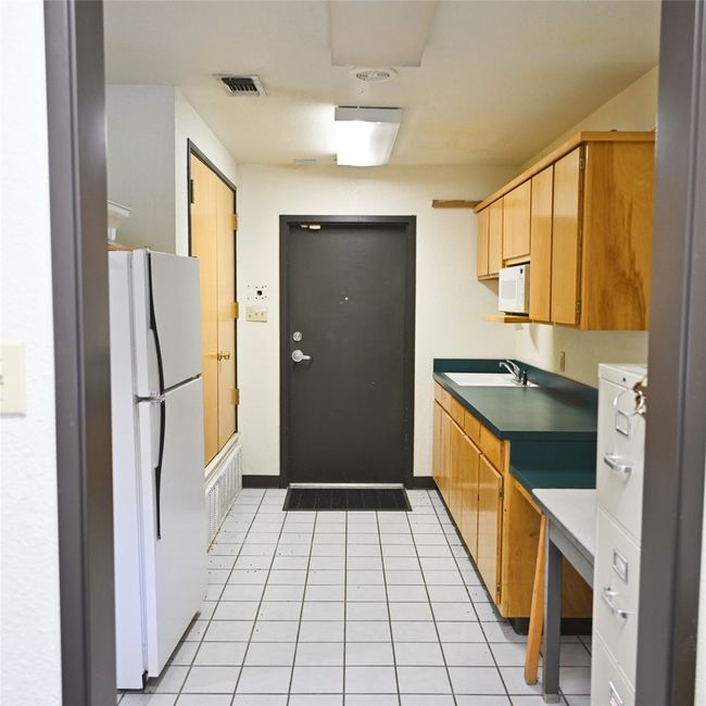 Kitchen featuring white appliances, dark countertops, and light tile patterned flooring | Image 14