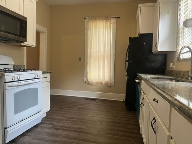 Kitchen with gas range gas stove, stainless steel microwave, dark wood-style flooring, white cabinetry, and dishwashing machine | Image 10
