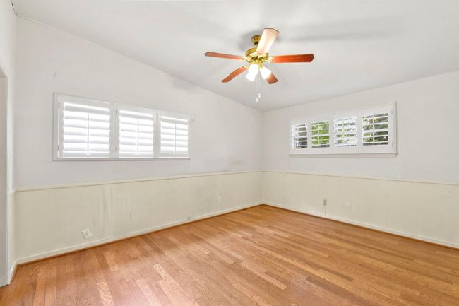 Spacious primary bedroom with elegant wood flooring, abundant natural light, and classic ceiling fan. | Image 19