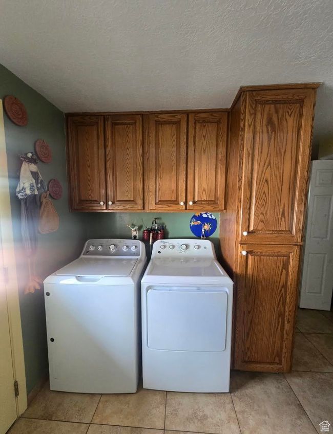 Laundry area with washing machine and clothes dryer, cabinet space, a textured ceiling, and light tile patterned floors | Image 9