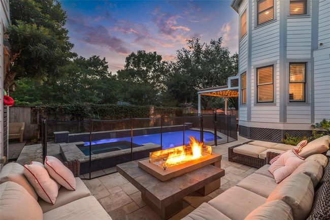 This backyard oasis features a cozy seating area with a modern fire pit, a pool and spa (with removable child fence), and lush greenery, perfect for relaxing and entertaining. | Image 32