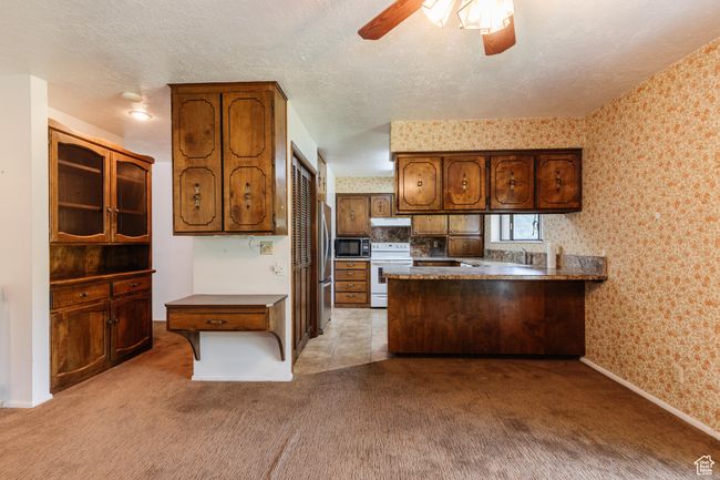 Kitchen featuring stainless steel appliances, wallpapered walls, a peninsula, light carpet, and ceiling fan | Image 7
