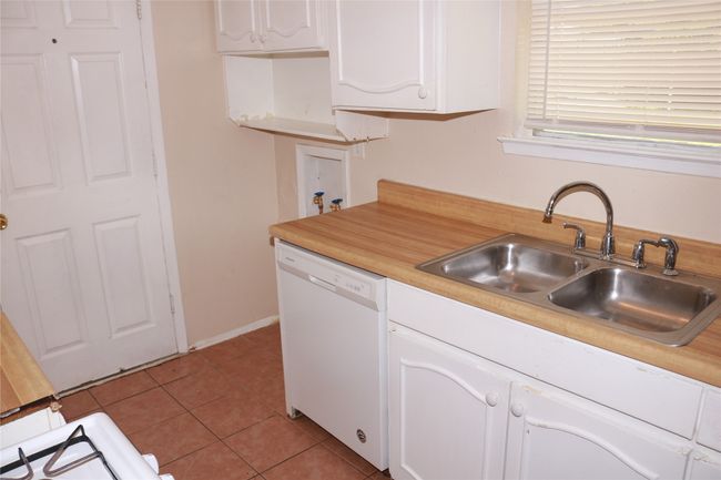 Kitchen with white dishwasher, a sink, white cabinetry, light countertops, and light tile patterned floors | Image 12