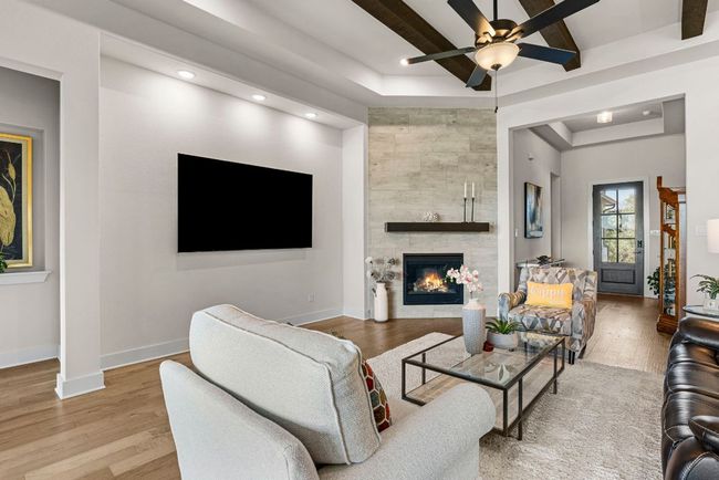Living room with a tray ceiling, beam ceiling, light wood-type flooring, baseboards, and a tile fireplace | Image 13