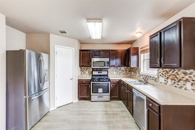 Kitchen featuring stainless steel appliances, dark brown cabinets, tasteful backsplash, light countertops, and light wood-type flooring | Image 8