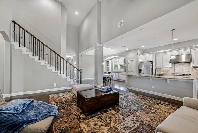 Living room with decorative columns, dark wood-style flooring, arched walkways, a towering ceiling, and stairway | Image 7