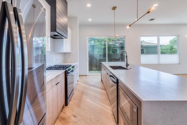 Kitchen with black appliances, modern cabinets, decorative backsplash, light countertops, and light wood-style flooring | Image 11