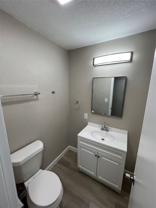 Half bath with wood finished floors, vanity, toilet, a textured ceiling, and baseboards | Image 18