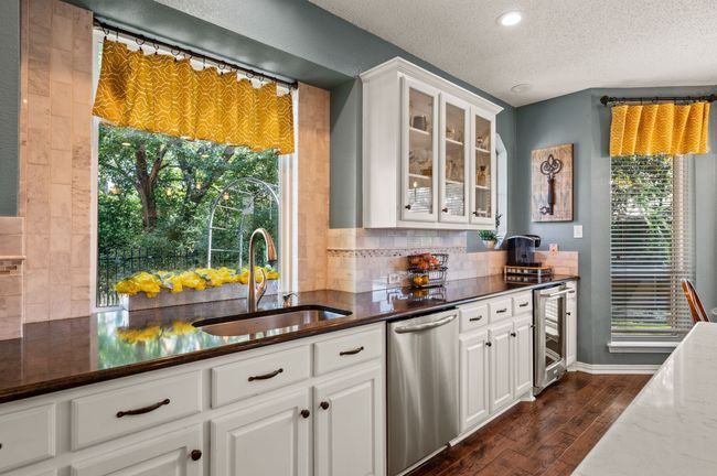Kitchen with glass insert cabinets, white cabinets, stainless steel dishwasher, dark wood finished floors, and a textured ceiling | Image 15