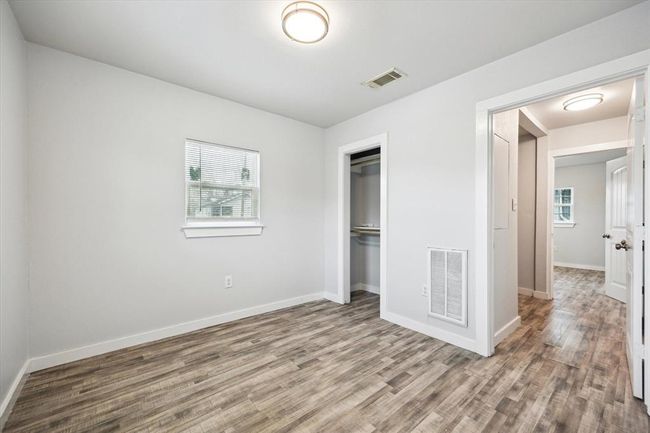 This photo showcases a bright, freshly painted room with wood-style flooring, a small window, a closet, and recessed lighting, offering a clean and modern look. Ideal for a bedroom or office space. | Image 7