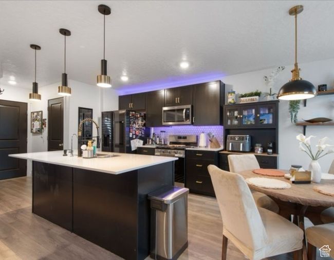 Kitchen with appliances with stainless steel finishes, light wood-type flooring, light countertops, a kitchen island with sink, and tasteful backsplash | Image 6