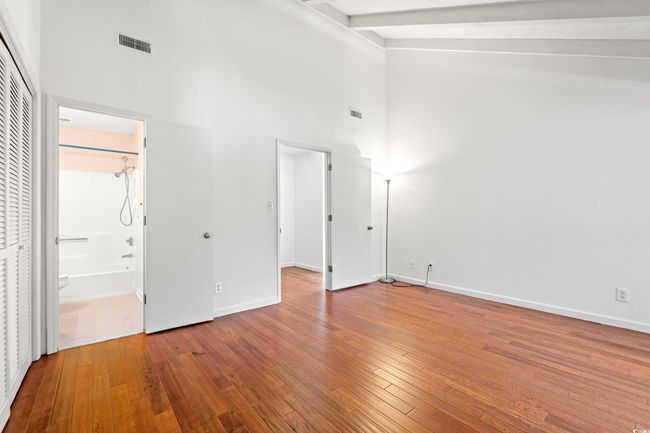 Unfurnished bedroom with high vaulted ceiling, hardwood / wood-style flooring, beamed ceiling, and connected bathroom | Image 14