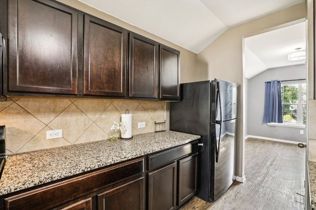 Kitchen with vaulted ceiling, freestanding refrigerator, dark brown cabinets, light stone counters, and backsplash | Image 5