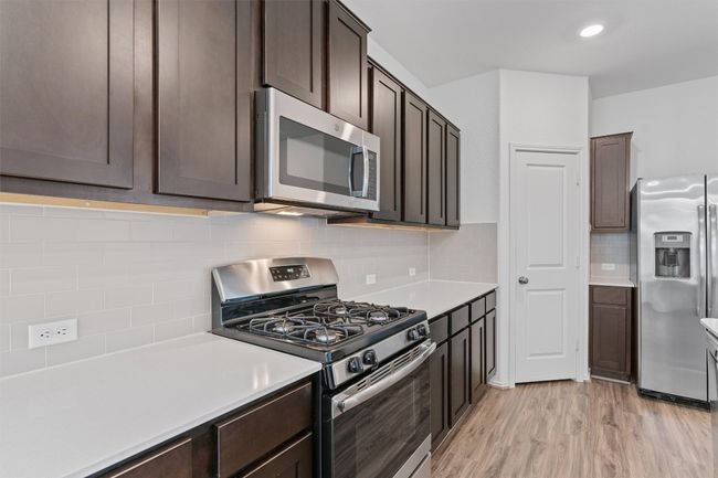 Kitchen featuring light wood finished floors, stainless steel appliances, dark brown cabinets, and light countertops | Image 8