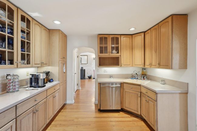 Kitchen featuring glass insert cabinets, light wood-style floors, arched walkways, dishwasher, and a sink | Image 17