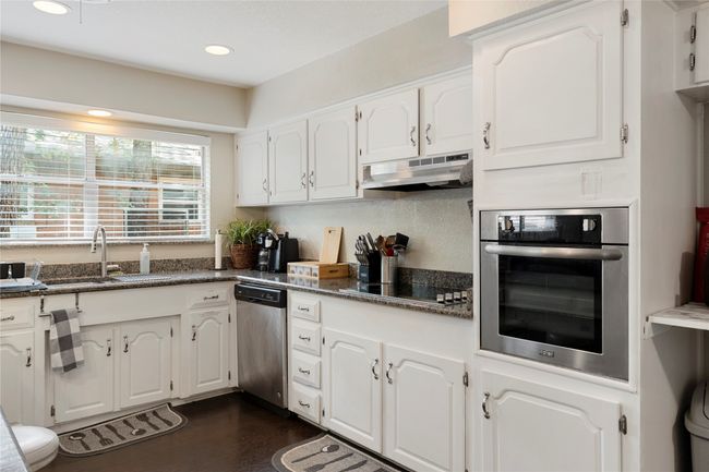 Kitchen featuring appliances with stainless steel finishes, under cabinet range hood, a sink, white cabinets, and dark wood-style floors | Image 7