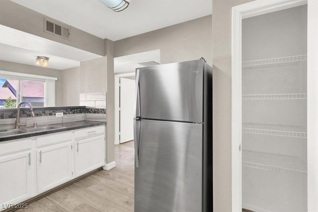Kitchen with dark countertops, a sink, white cabinets, visible vents, and freestanding refrigerator | Image 11