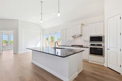 Kitchen with decorative backsplash, white cabinetry, appliances with stainless steel finishes, light hardwood / wood-style floors, and extractor fan | Image 2