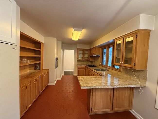 Kitchen featuring tasteful backsplash, glass insert cabinets, white refrigerator, a sink, and a peninsula | Image 6