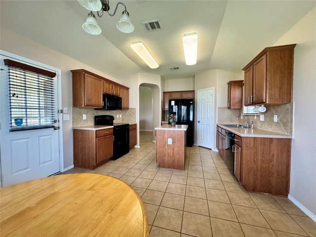 Kitchen with black appliances, arched walkways, backsplash, a center island, and light countertops | Image 4
