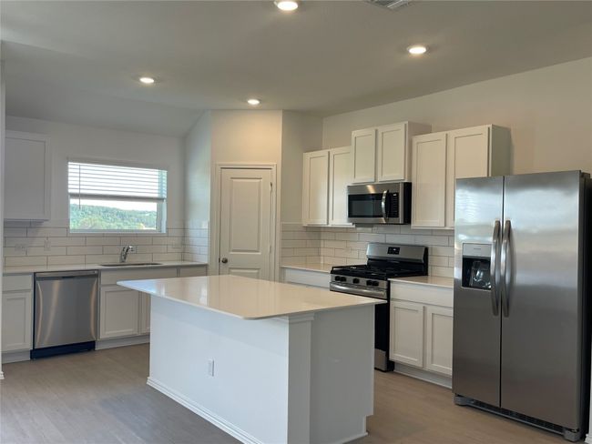 Kitchen featuring stainless steel appliances, a sink, a center island, light wood-style floors, and tasteful backsplash | Image 8