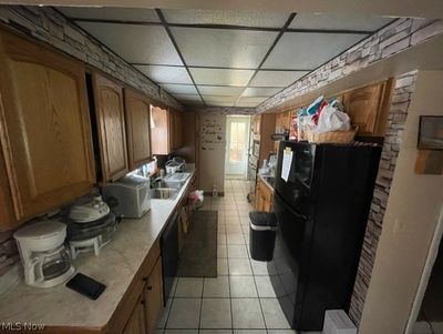 Kitchen with a drop ceiling, sink, light tile flooring, and black appliances | Image 3