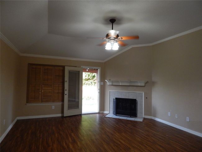 Unfurnished living room with wood finished floors, ceiling fan, vaulted ceiling, a tile fireplace, and ornamental molding | Image 7