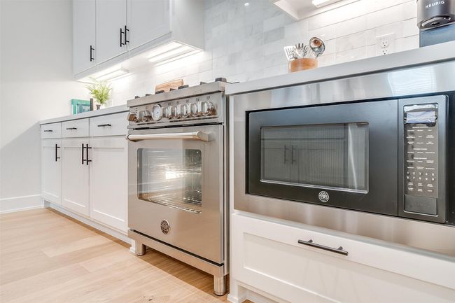 Interior details with backsplash, white cabinetry, light wood-type flooring, and high end stove | Image 11