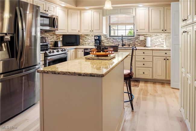 Kitchen with a center island, decorative backsplash, appliances with stainless steel finishes, and light stone countertops | Image 11