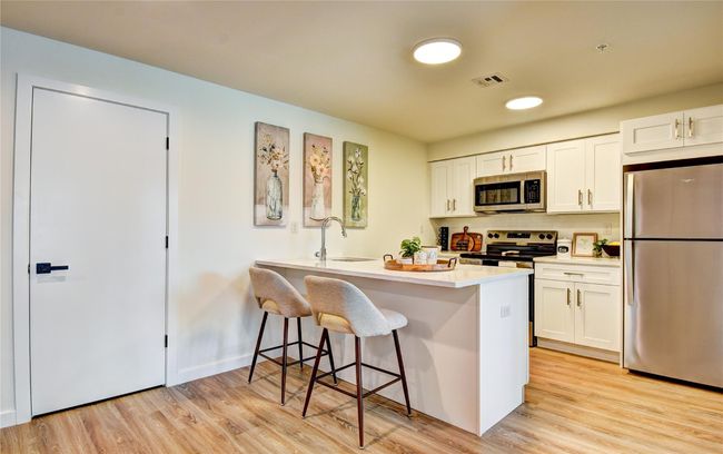 Kitchen with visible vents, a breakfast bar, appliances with stainless steel finishes, light wood-style floors, and white cabinets | Image 4