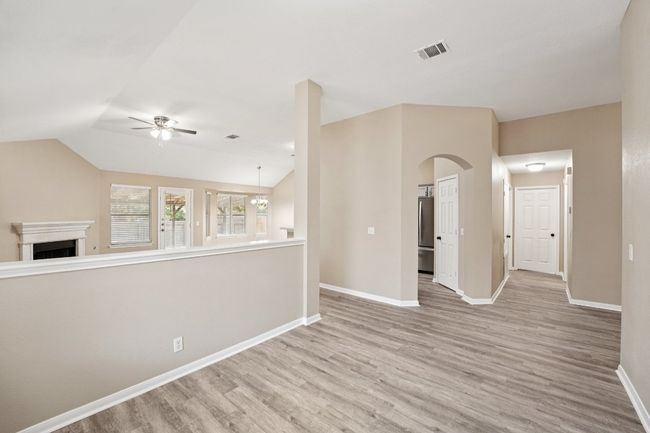 Unfurnished room featuring light wood-style flooring, vaulted ceiling, arched walkways, a fireplace, and ceiling fan | Image 25