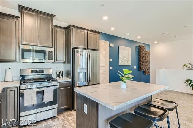 Kitchen featuring light stone countertops, dark brown cabinetry, a breakfast bar, appliances with stainless steel finishes, and a kitchen island | Image 18
