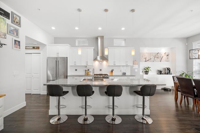 Kitchen featuring a sink, backsplash, high end fridge, wall chimney exhaust hood, and dark wood-style flooring | Image 9