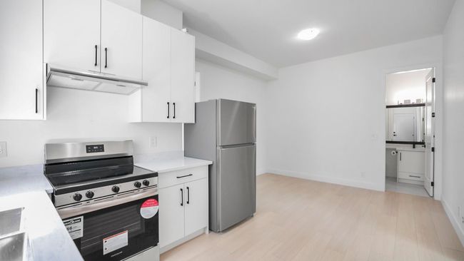 Kitchen featuring appliances with stainless steel finishes, ventilation hood, light countertops, white cabinets, and light wood finished floors | Image 19