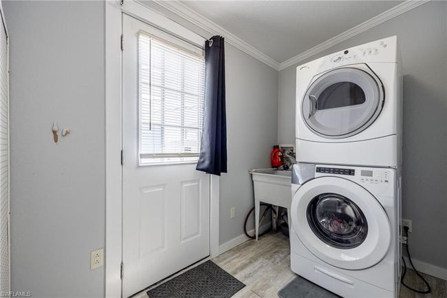 Clothes washing area with laundry area, light wood-style floors, baseboards, stacked washer and clothes dryer, and crown molding | Image 27
