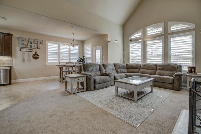 Living area with a chandelier, healthy amount of natural light, light colored carpet, vaulted ceiling, and light tile patterned floors | Image 12