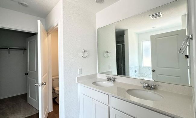 Bathroom featuring double vanity, wood finished floors, a shower stall, a walk in closet, and a textured wall | Image 7