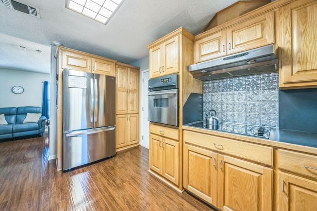 Kitchen with tasteful backsplash, visible vents, appliances with stainless steel finishes, under cabinet range hood, and dark wood-style floors | Image 13