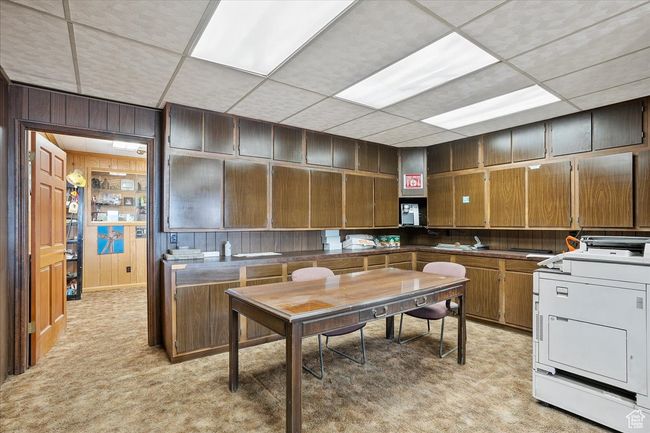 Kitchen featuring wooden walls, brown cabinetry, washer / dryer, a paneled ceiling, and light colored carpet | Image 17