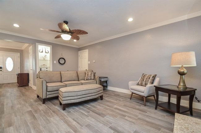 Another view of the living room- built in shelves with lighting, crown molding and ceiling fan plus wood look tile flooring throughout the foyer, kitchen, breakfast/dining and living room | Image 9